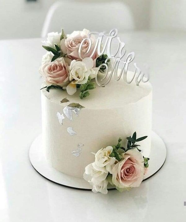 a white wedding cake with flowers and the word mr and mrs on top is sitting on a table