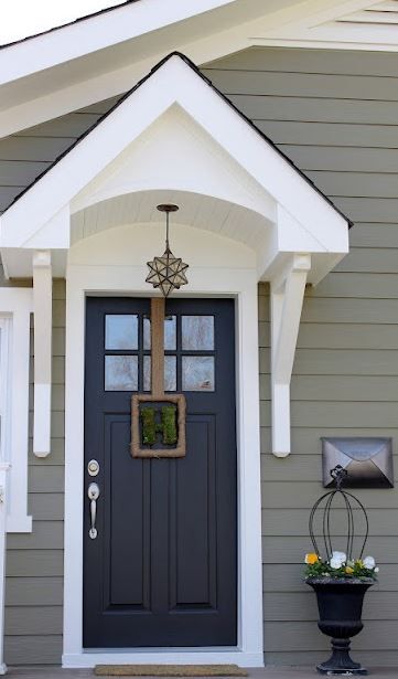 the front door of a gray house with white trim and two black planters on either side