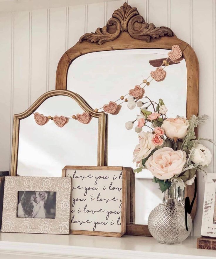 there is a mirror, vase with flowers and pictures on the mantle next to it