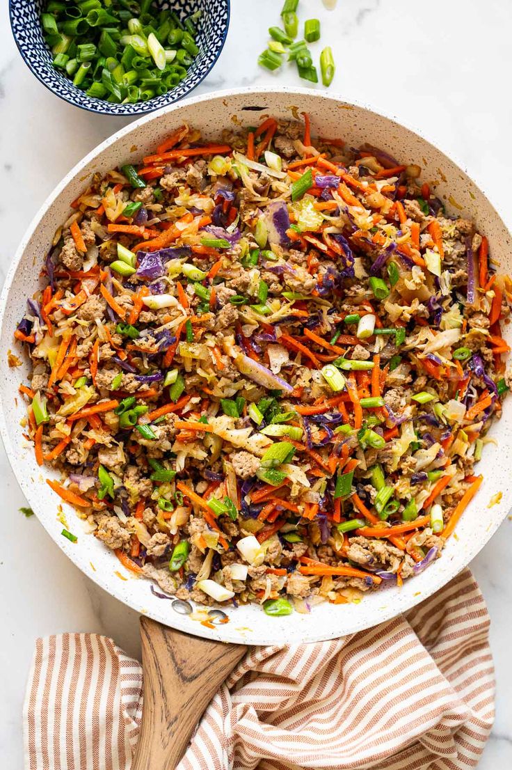 a pan filled with vegetables and meat on top of a white counter next to a wooden spoon