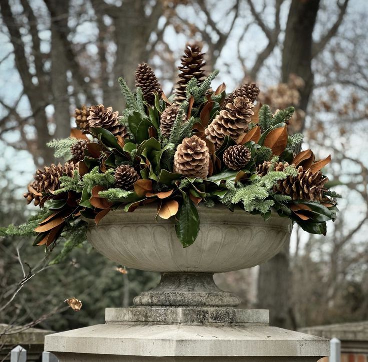 a planter filled with pine cones and greenery on top of a cement pedestal