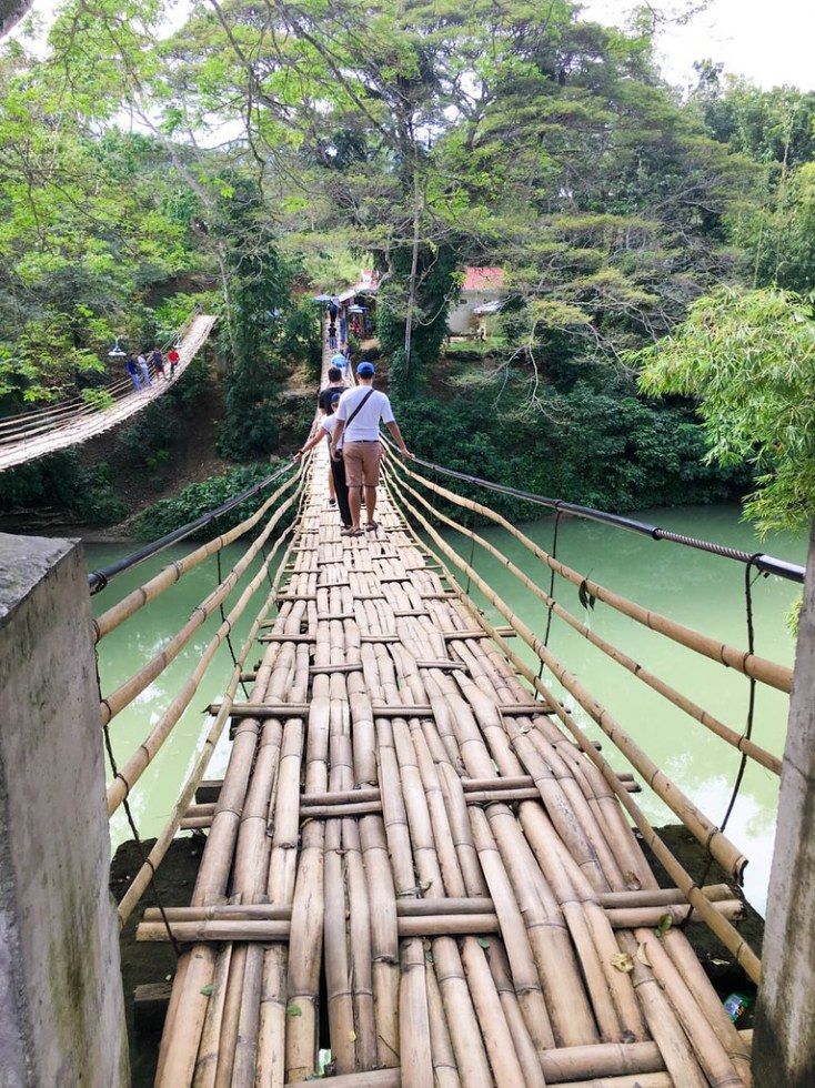 a man walking across a bamboo bridge over water