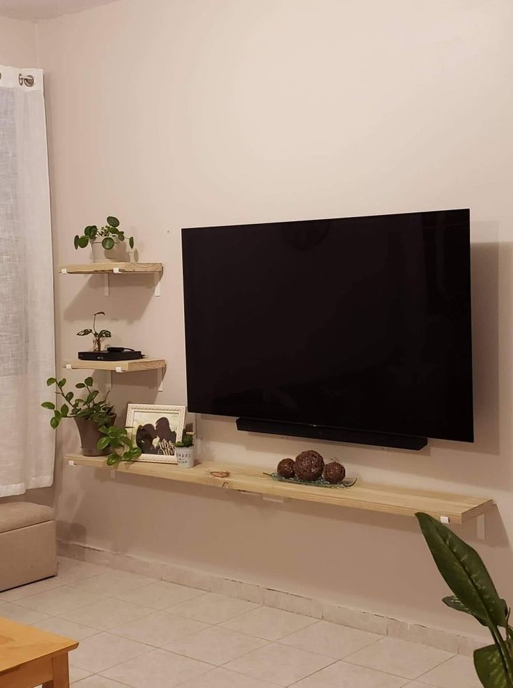 a flat screen tv sitting on top of a wooden shelf in a living room next to a window