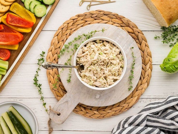 a bowl of tuna salad next to sliced cucumbers and other vegetables on a table