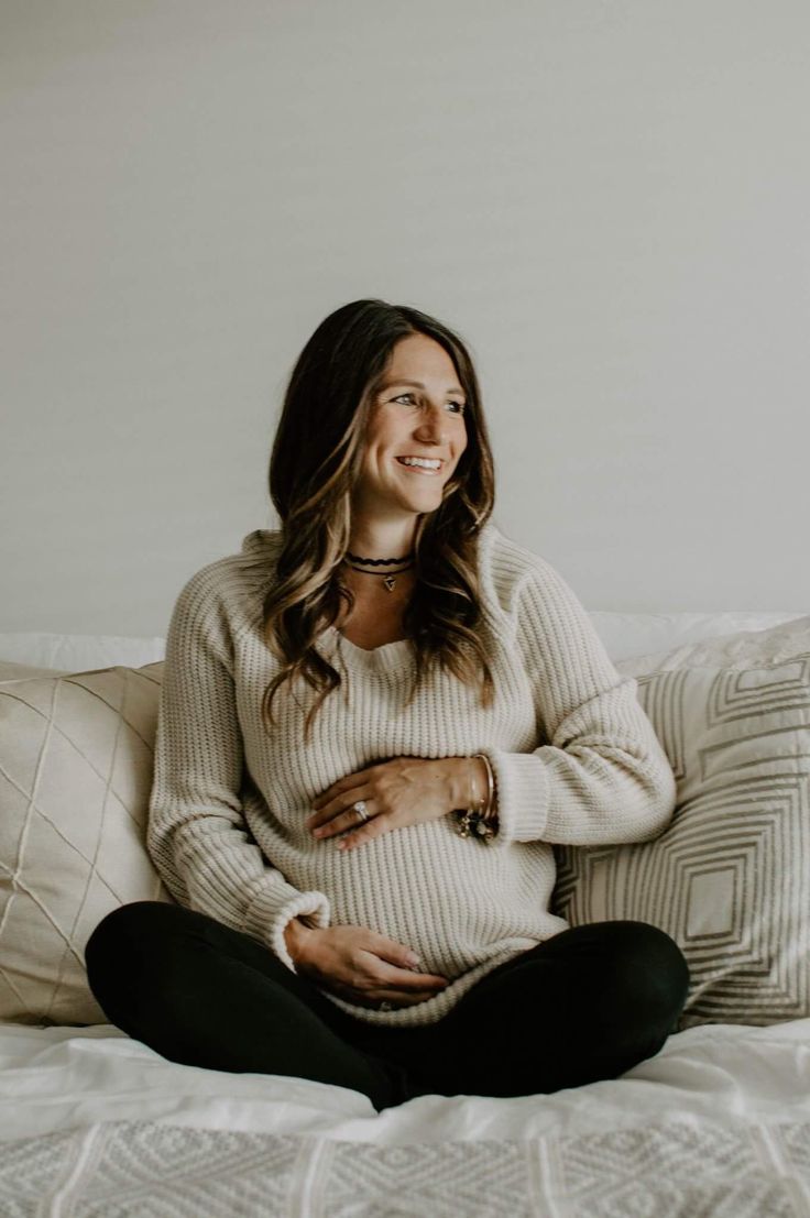 a pregnant woman sitting on a bed with her belly tucked under her stomach and smiling at the camera