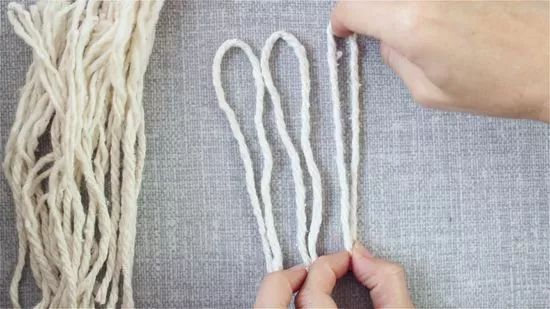 two hands are working on some white string with scissors and yarn in front of them