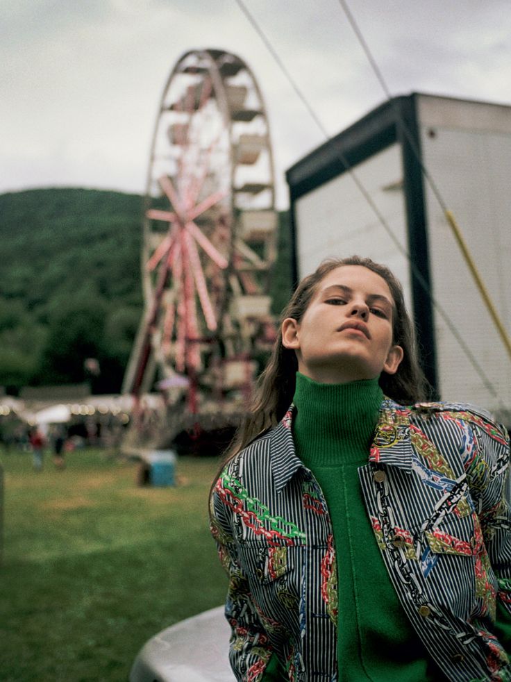 a woman sitting on the hood of a car in front of a carnival ferris wheel