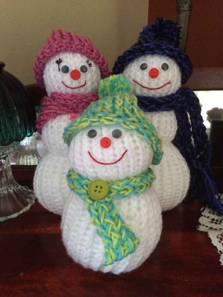 three crocheted snowmen with hats and scarves on top of a table