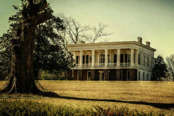 an old house in the middle of a field with a large tree on one side