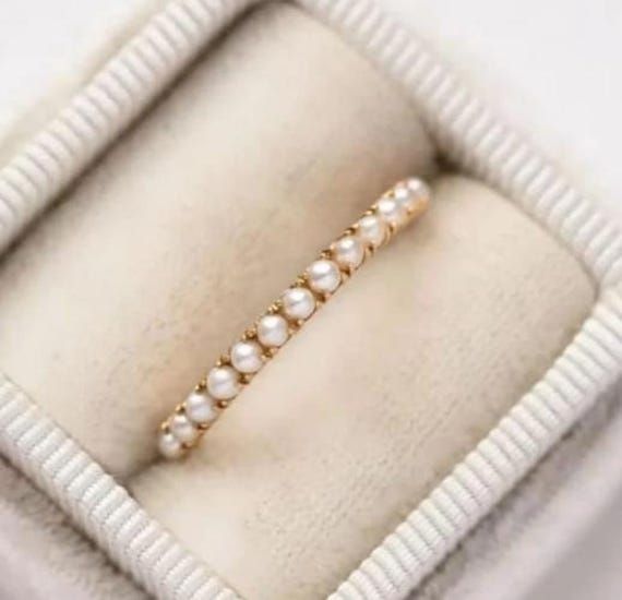 an open ring with pearls in it sitting on a white cushioned box that is filled with jewelry