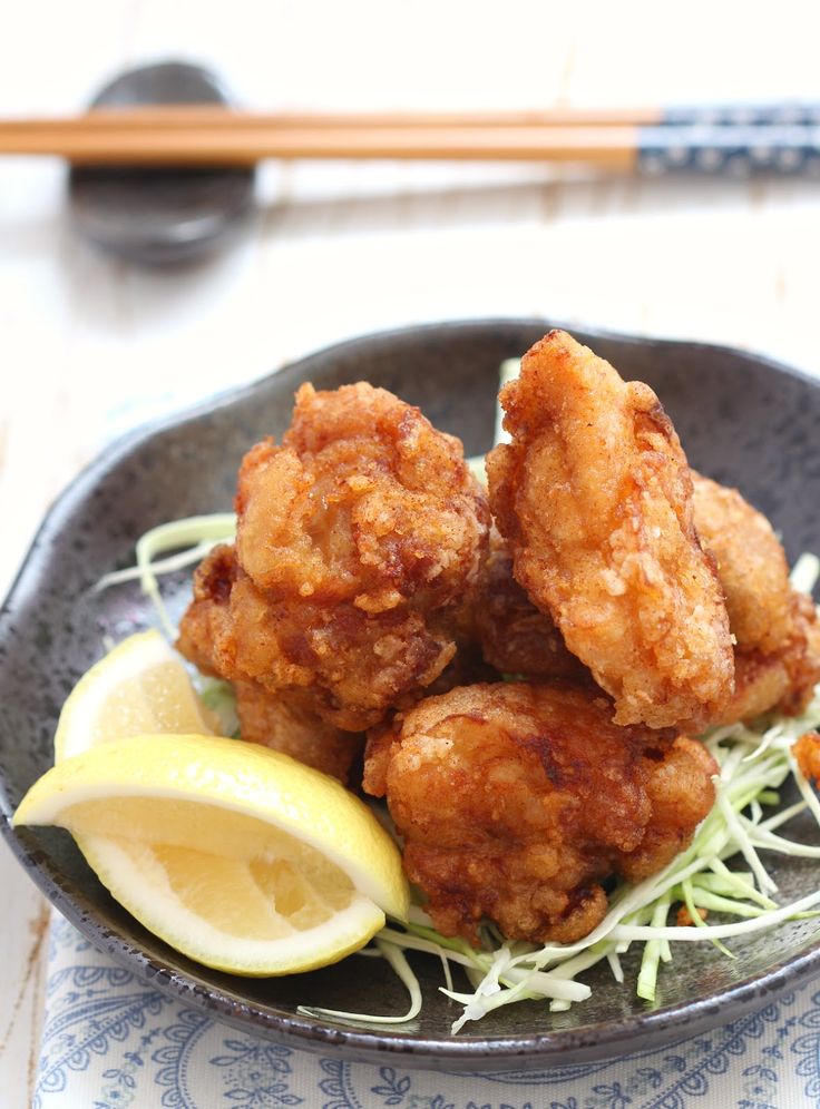 a plate with some fried food on it and lemon wedges next to the bowl