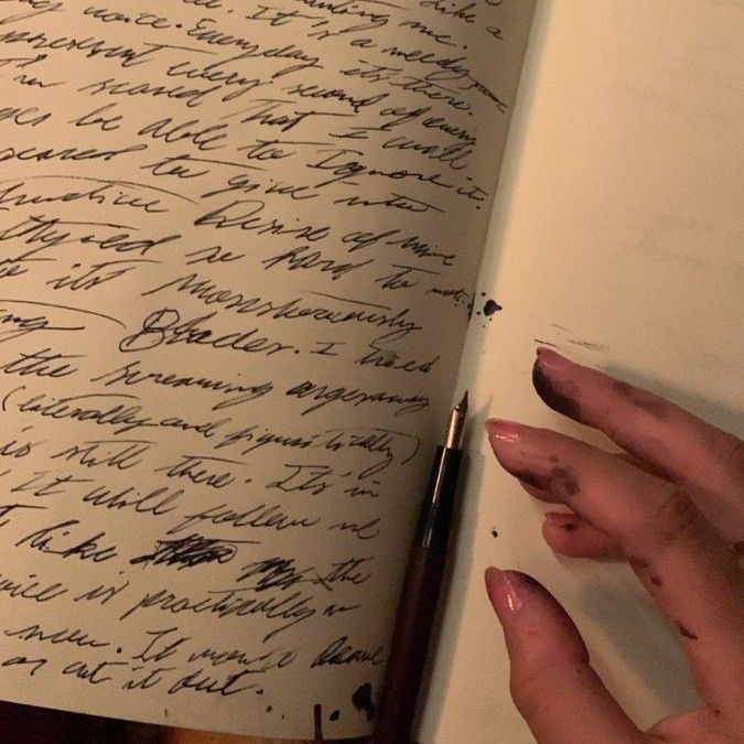 a hand holding a pen over a book with writing on the pages in cursive ink