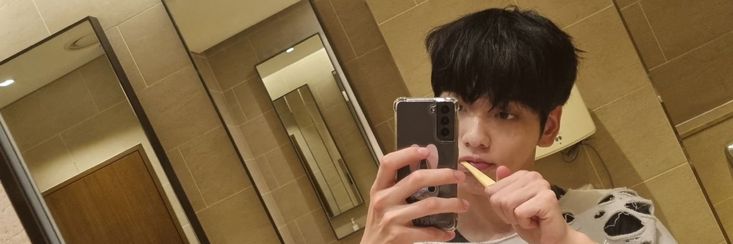 a young man taking a selfie in front of a mirror while brushing his teeth