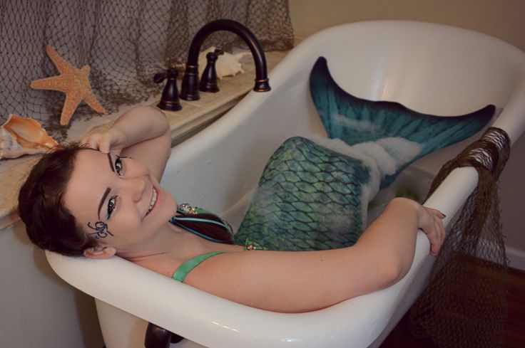 a woman laying in a bathtub with a mermaid tail on the back of it