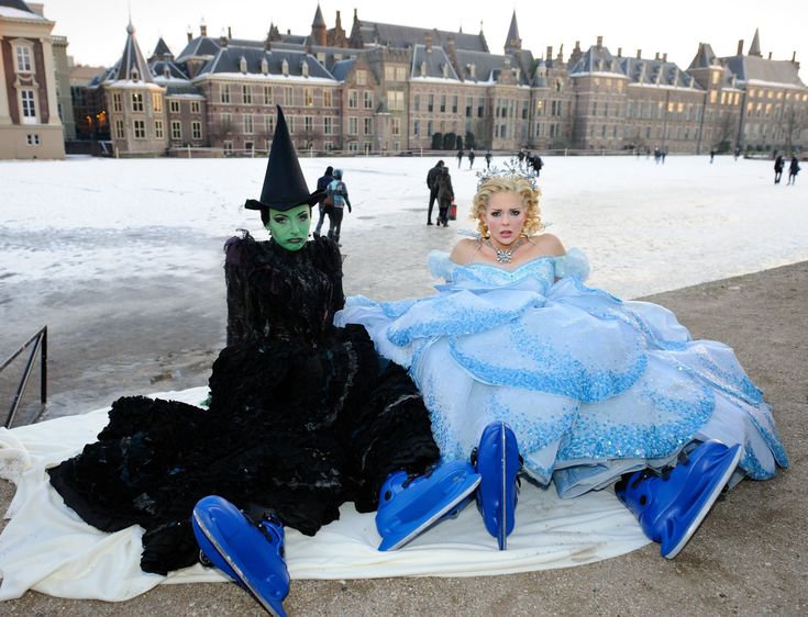 two women dressed up as witches sitting on a blanket in front of an old building