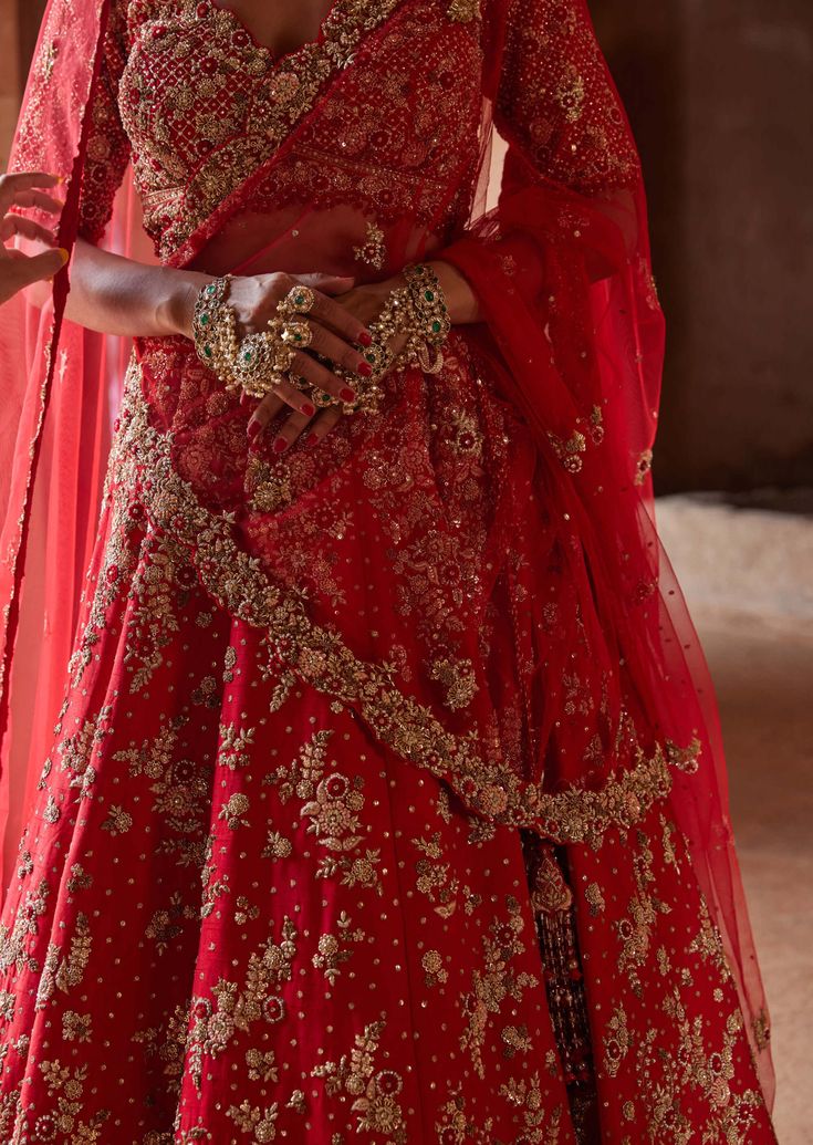 a woman in a red and gold bridal gown standing with her hands on her hips