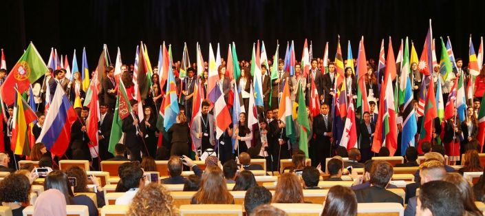 a group of people standing in front of rows of desks with flags on them