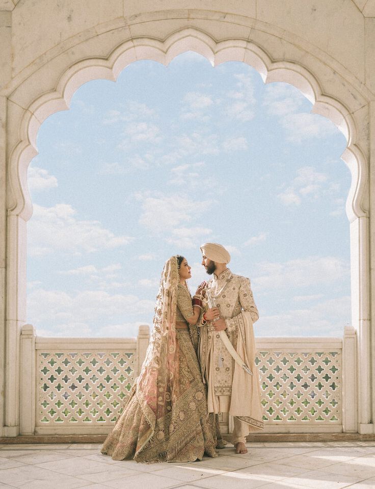 two people standing next to each other in front of a white arch and blue sky