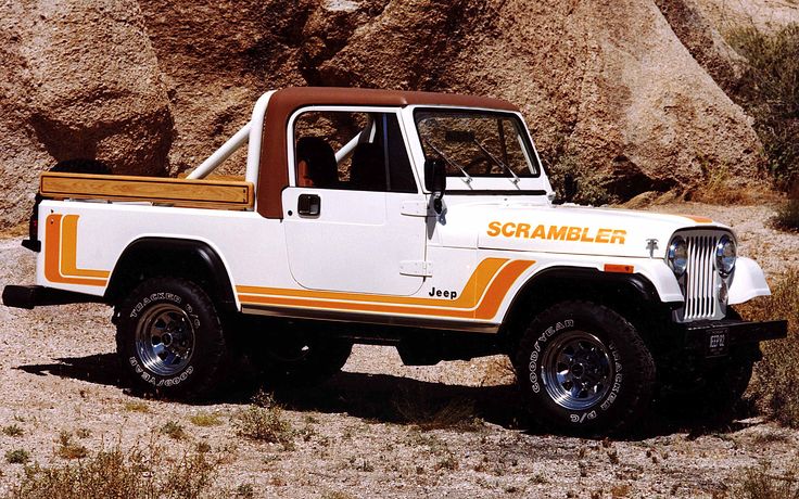 a white and orange jeep parked in the desert with rocks on the side behind it