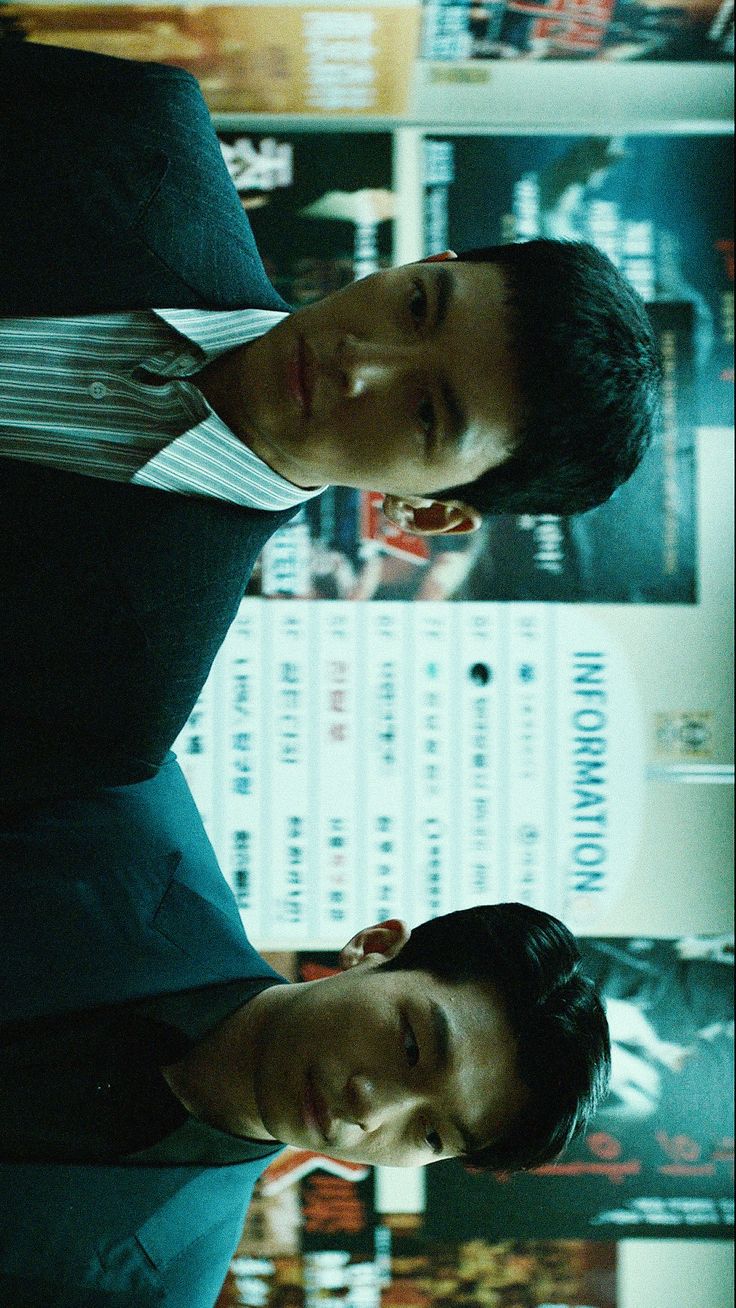 two men standing next to each other in front of a wall with posters on it