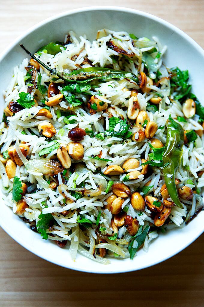 a white bowl filled with rice, nuts and broccoli on top of a wooden table