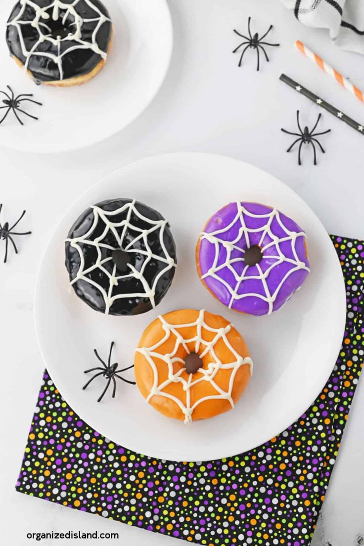 three decorated donuts on a plate with sprinkles and spider web decorations