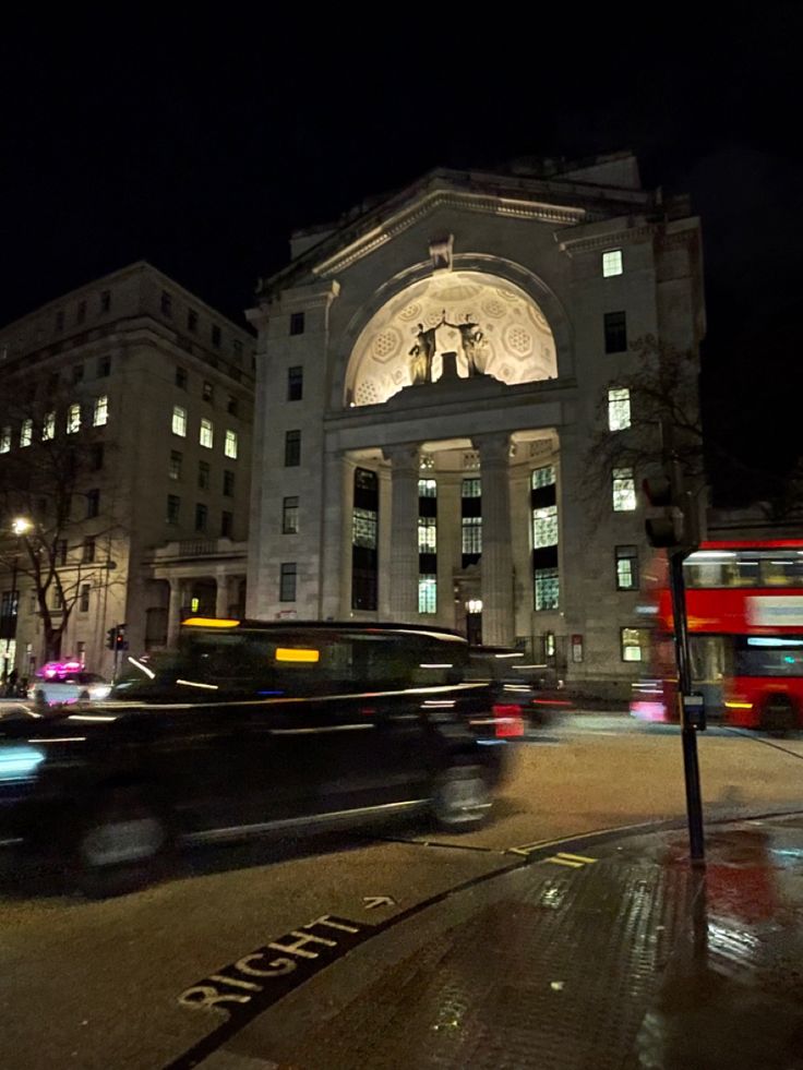 a city street at night with double decker buses and cars passing by on the road