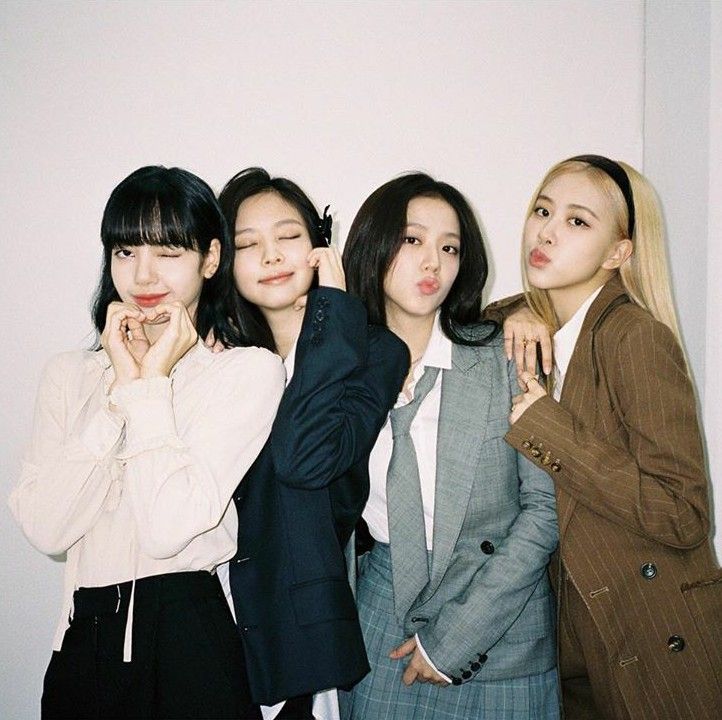 four young women standing next to each other in front of a white wall with their hands on their mouths