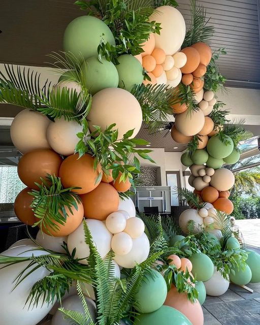 an arrangement of balloons and greenery hanging from the ceiling in front of a house