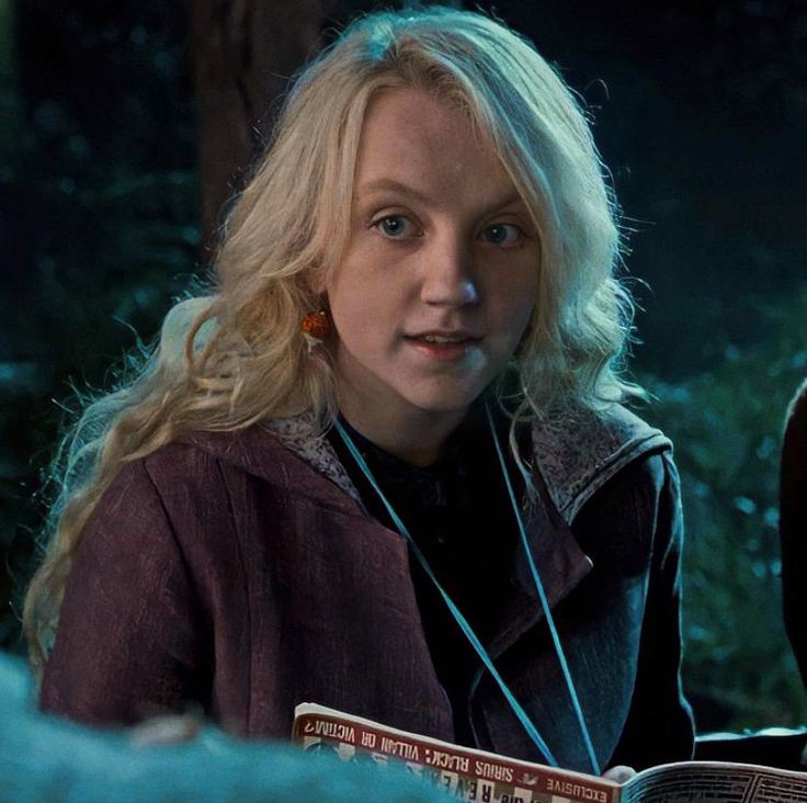 a woman with blonde hair is reading a book in the dark, and looking at the camera