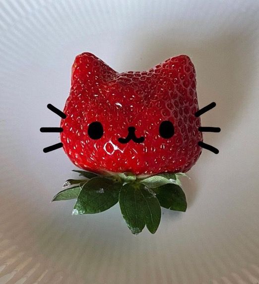 a strawberry shaped like a cat sitting on top of a green leafy plant with black eyes