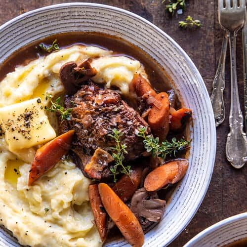 two bowls filled with mashed potatoes and carrots next to silverware on a wooden table