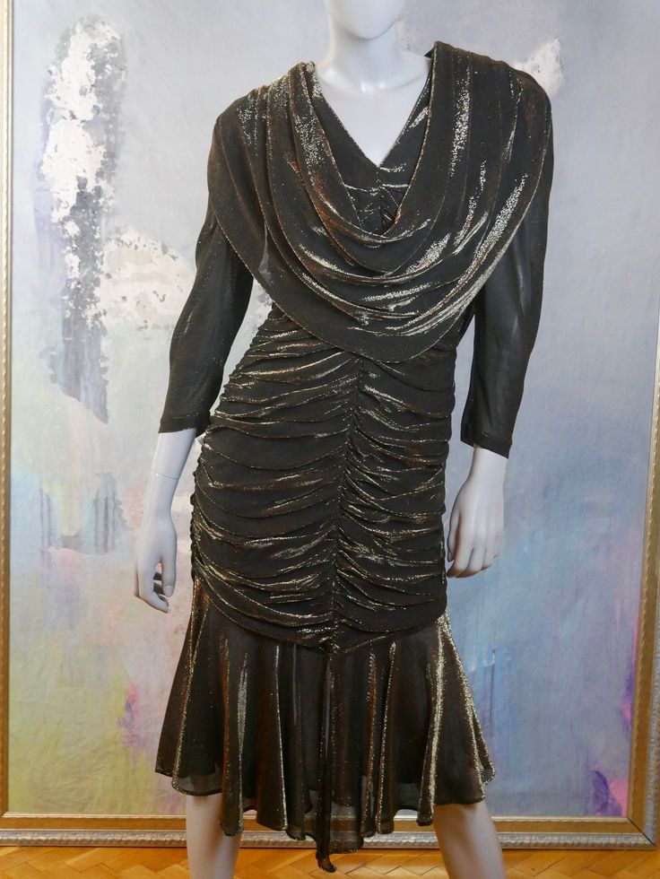 This 1980s glitter dress shimmers with gold on a black background. The stunning Austrian vintage dress has a V neckline, padded shoulders, bracelet-length sleeves, and a goddess folds yoke that drapes over the front and back to waist length The dress has a fitted waistline that gives way to a goddess pleated slimline fall to just below the hip line, where an 11-inch (27.94cm) softly ruffled panel falls to the hemline. The dress is lined in a black satin viscose fabric, and a long back zipper mak Vintage V-neck Party Dress, Glittering Gold Evening Dress, Gold Glitter Evening Dress, Vintage Gold Evening Dress For Gala, Vintage Evening Dresses For Festive Season, Vintage Gala Dresses For Party Season, Vintage Gold Evening Dress For Party, Vintage Dresses For Gala, Vintage Festive Evening Dress For Party