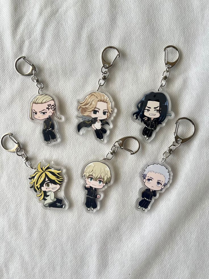 six keychains with cartoon characters on them sitting on a white sheet, one has a black cat and the other has blonde hair