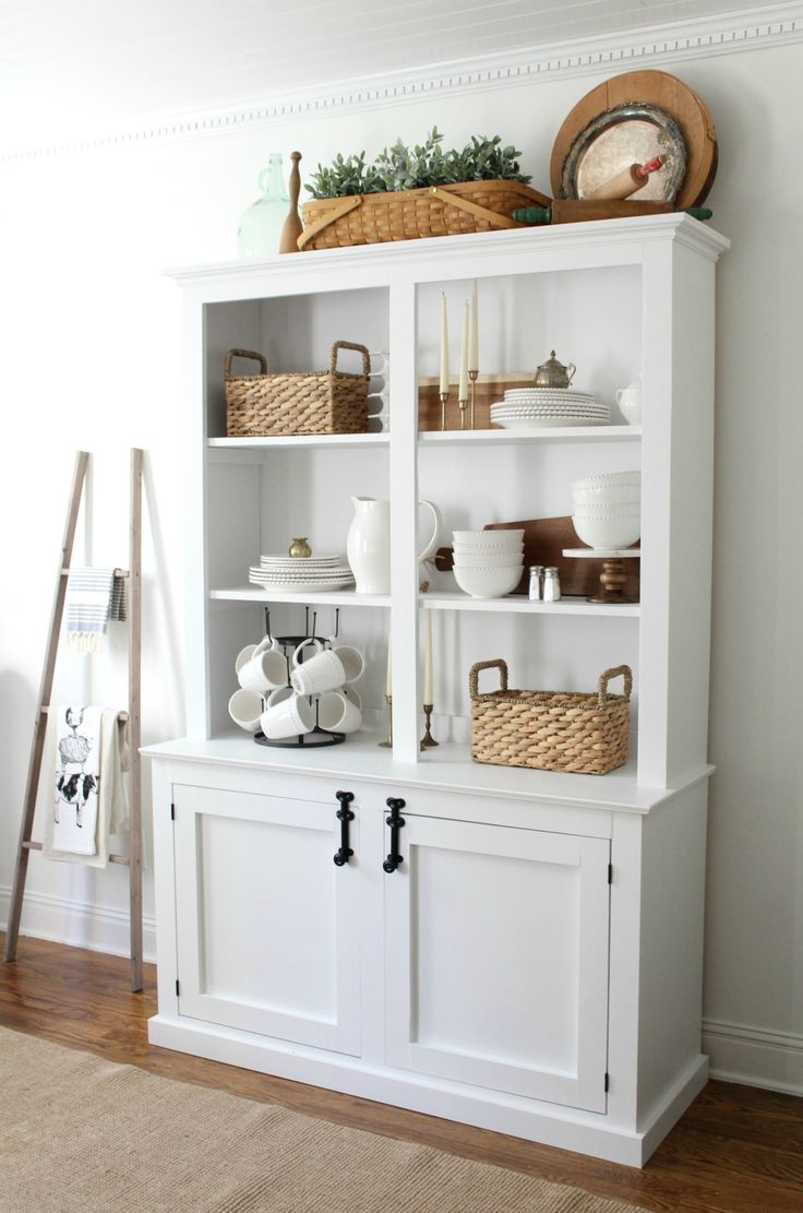 a white bookcase with baskets and dishes on top, sitting next to a wall