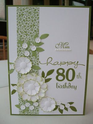 a birthday card with white flowers and green trimmings on the front, sitting on a table