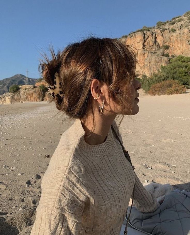 a woman sitting on the beach with her hair in a bun and leopard print earring