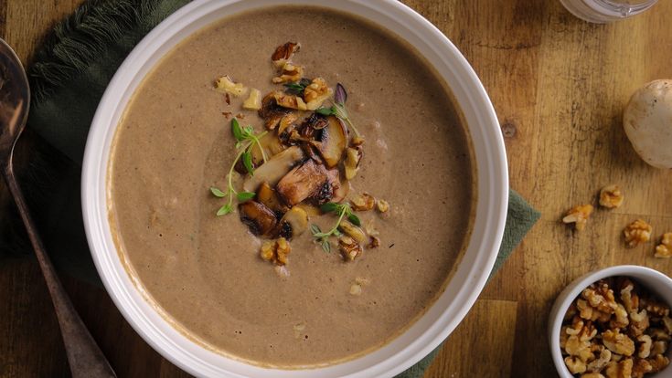 a white bowl filled with soup next to a spoon and some nuts on a wooden table