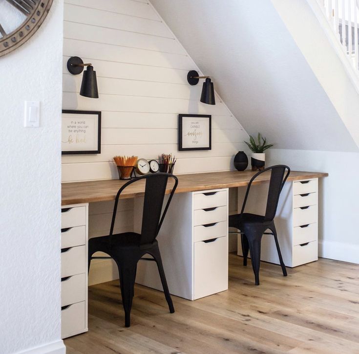 a desk with two chairs and a clock on the wall above it in a white room