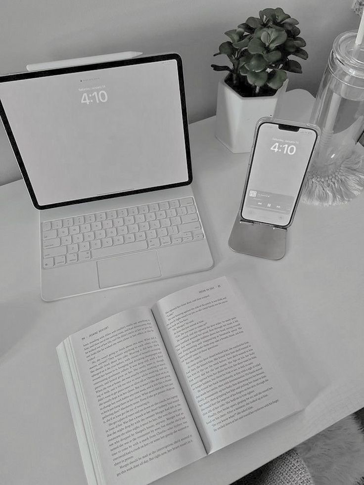 an open laptop computer sitting on top of a desk next to a phone and book