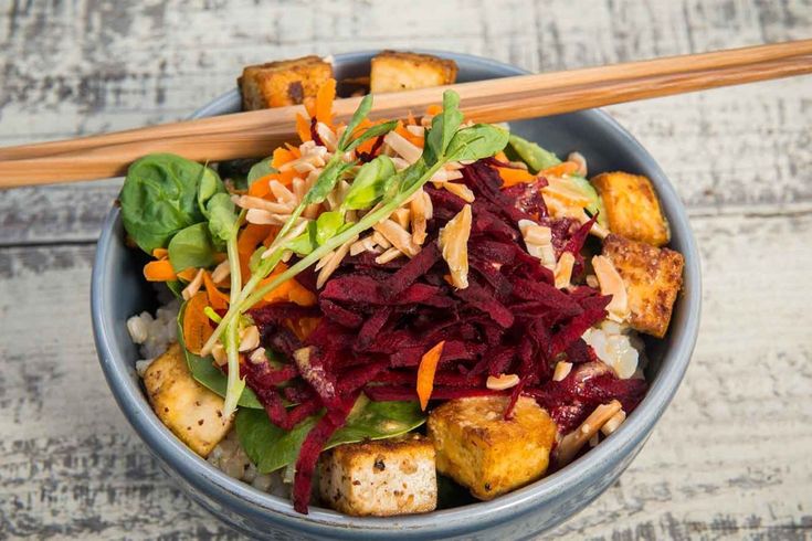 a bowl filled with vegetables and tofu on top of a wooden table next to chopsticks