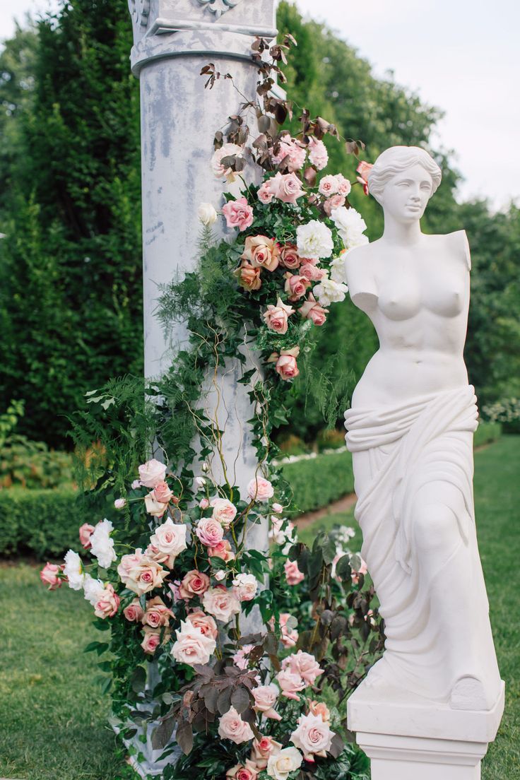 a white statue sitting next to a flower covered pole