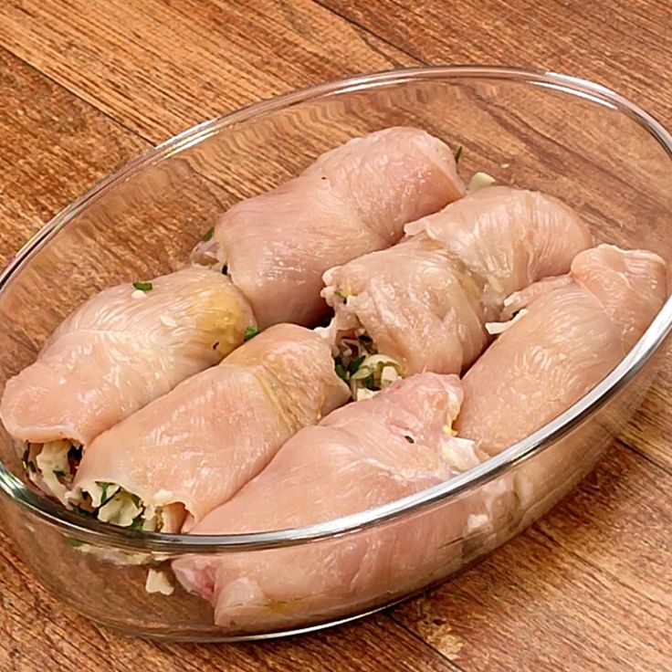 some raw chicken in a glass bowl on a wooden table