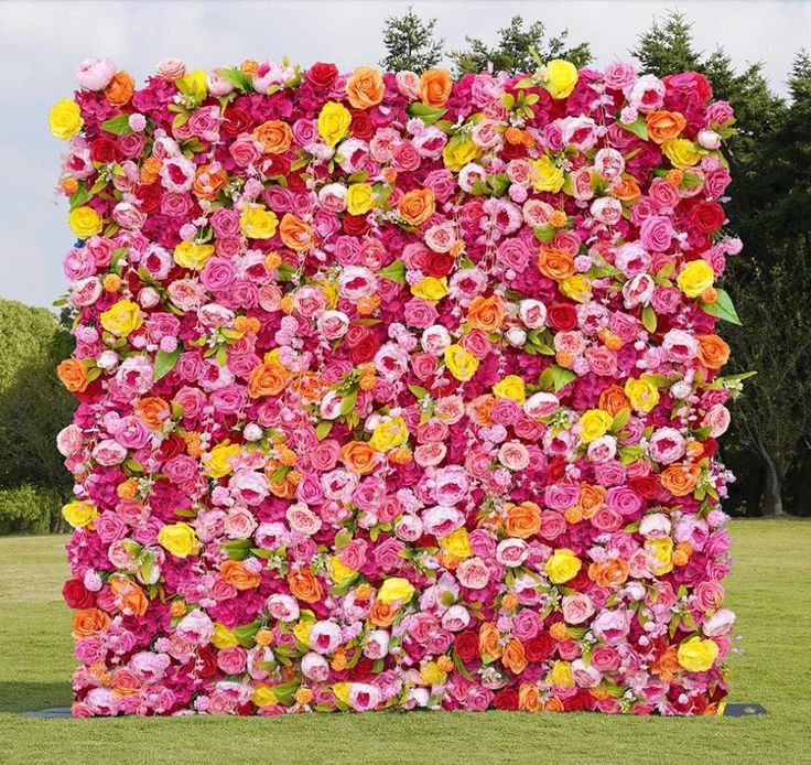 a large flowered wall in the middle of a field with lots of pink and yellow flowers