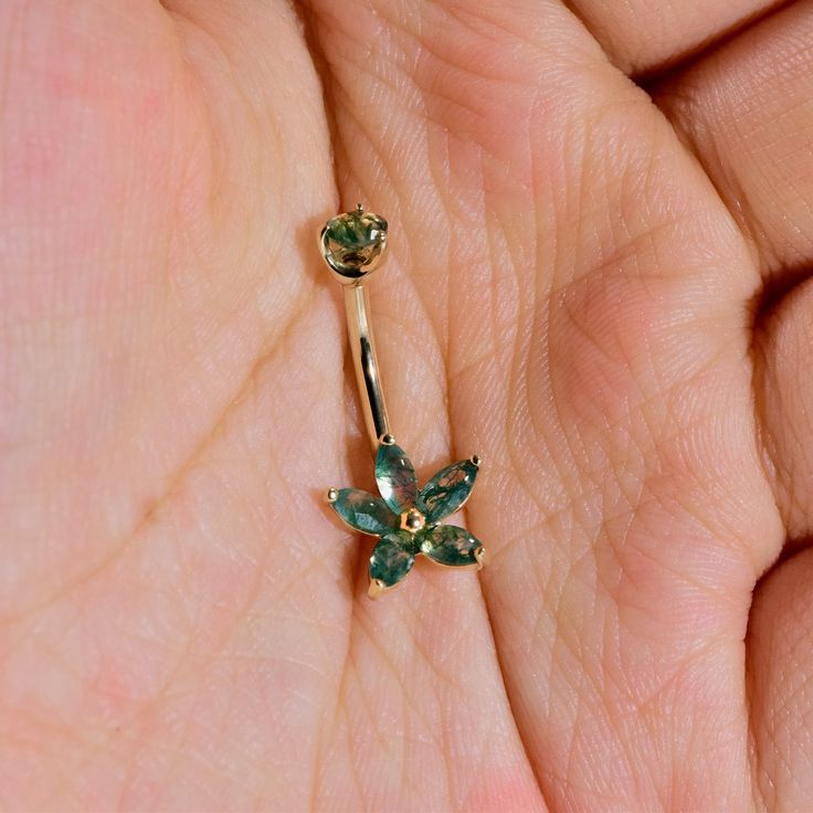 a close up of a person's hand holding a ring with green stones on it