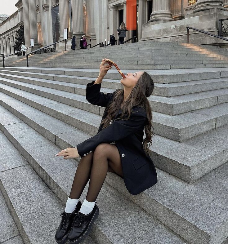 a woman is sitting on the steps drinking from a bottle in front of a building