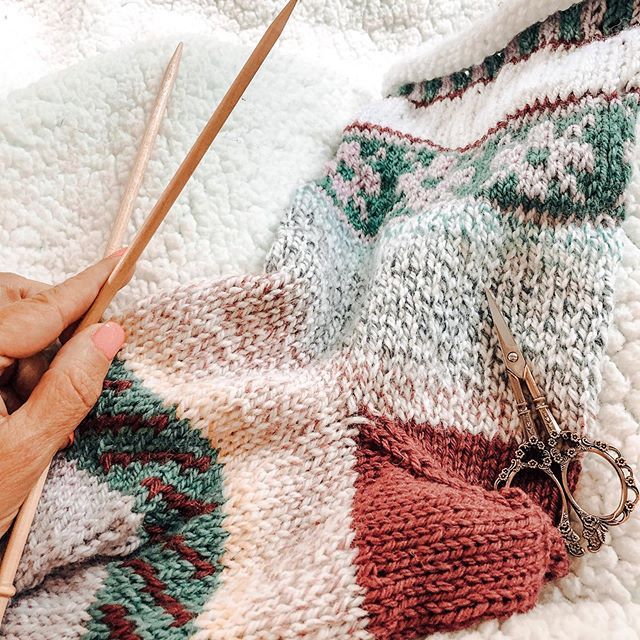 a person is knitting on a blanket with scissors in their hand and another pair of yarns next to them