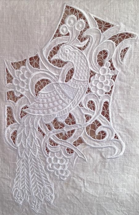 a white piece of cloth with an embroidered bird on it's back and some leaves in the middle