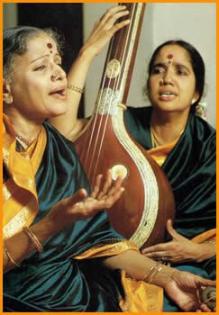 two women are sitting and one is holding a musical instrument