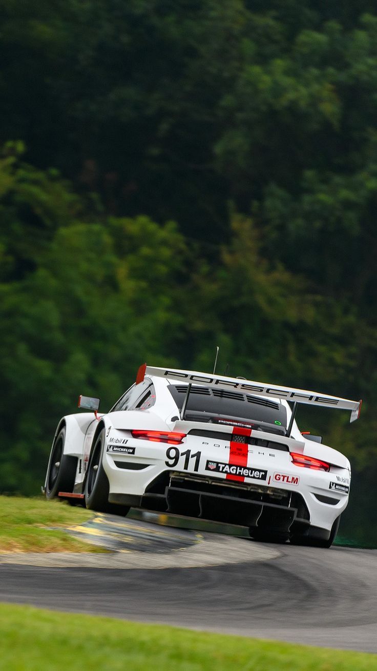 a white sports car driving on a race track with trees in the backgroud